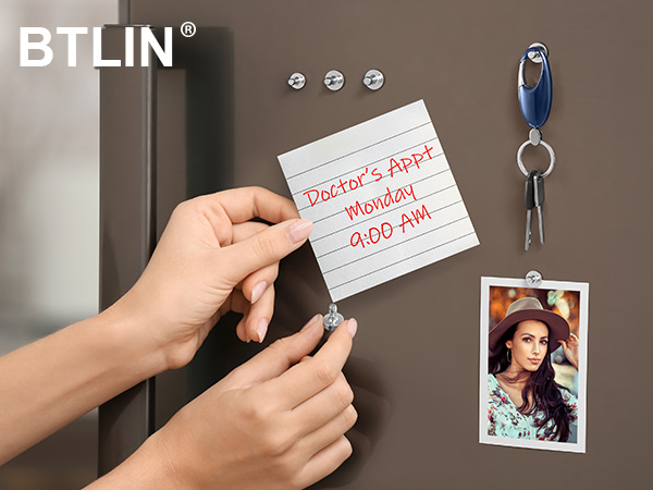 Magnetic note being placed on refrigerator surface with handwritten appointment reminder. Blue keychain and photo visible on magnetic surface.