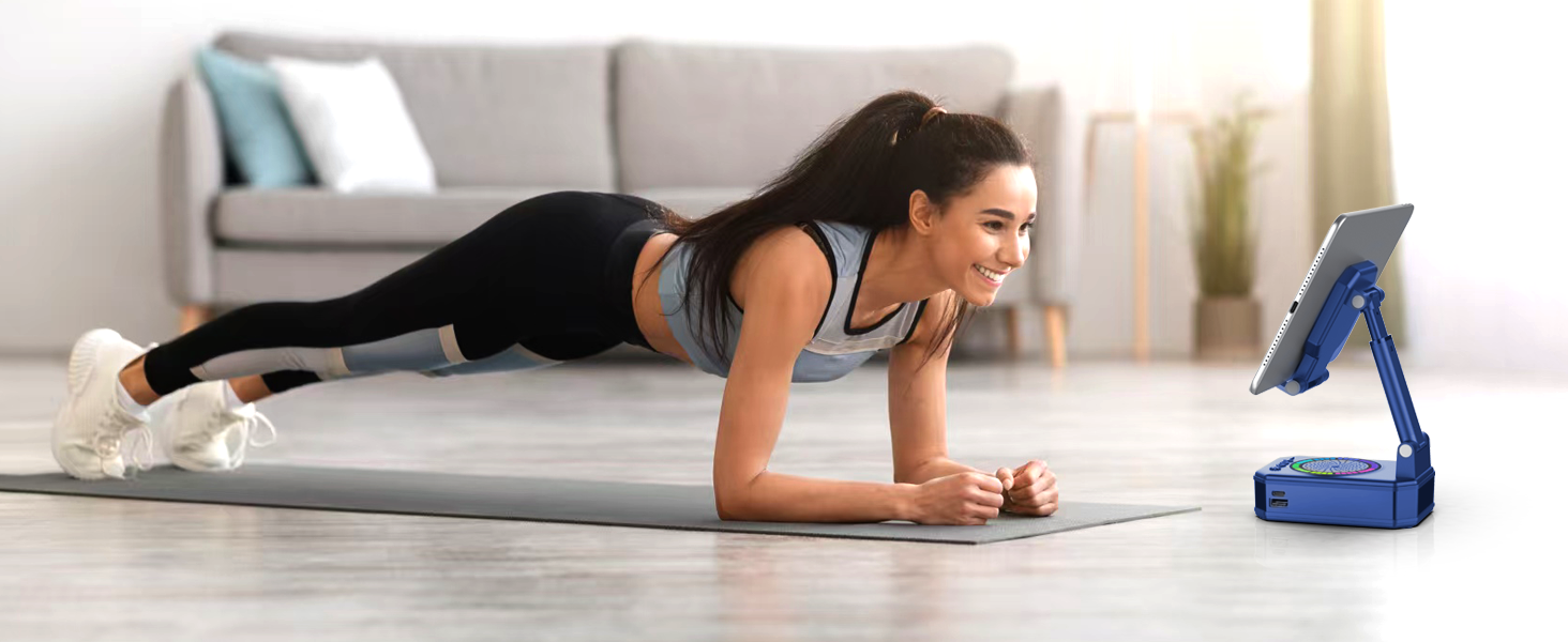 Person performing plank exercise position on exercise mat, with blue fitness device propped up nearby for viewing content during workout.