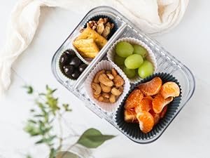 Silicone baking cups of various sizes in a lunch box sorting fruits, nuts, crackers
