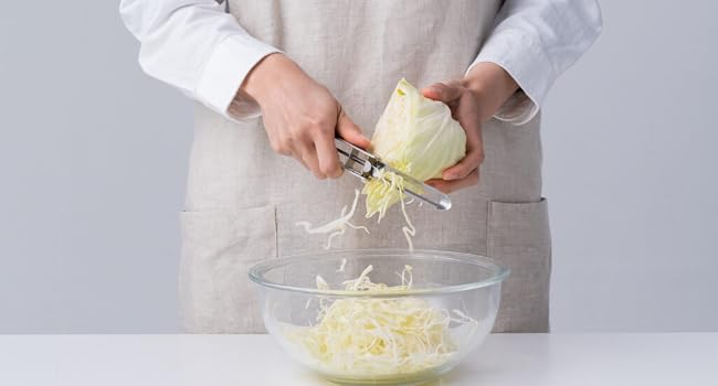 Person shredding cabbage into a glass bowl