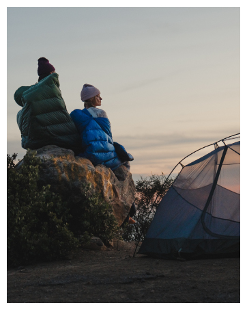 Man and female sitting on rock in sleeping bags next to Marmot tent at dusk