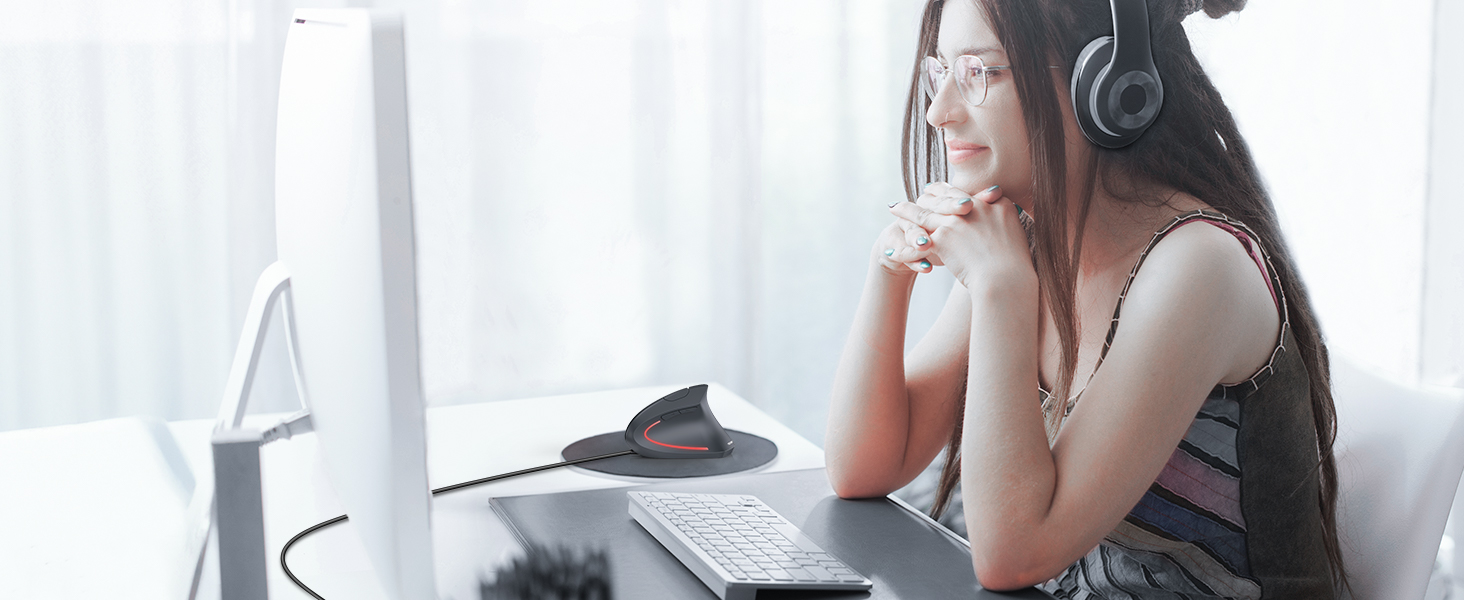 Person wearing headphones sitting at desk with computer monitor, appearing to be in a contemplative pose while working.