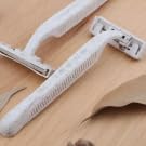 2 white disposable razors with textured handles and protective blade covers on light wooden surface