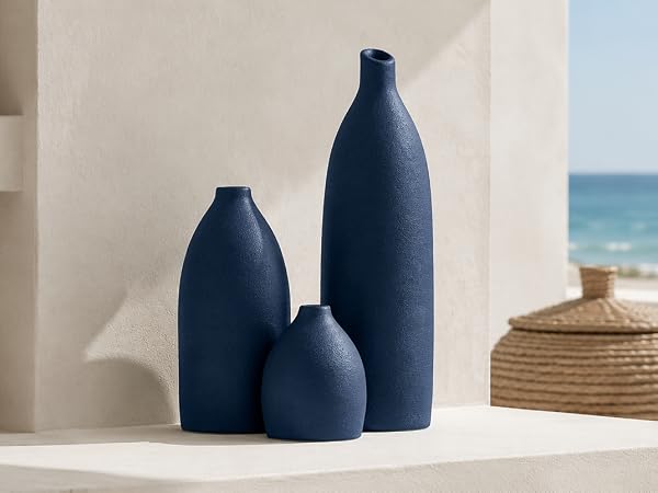 Three-piece navy blue textured vase set on a coastal shelf with woven decor and sea view.