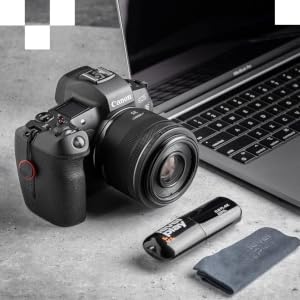Canon DSLR camera with attached lens next to laptop, USB drive, and memory card. Camera features visible controls and prominent lens, showcasing professional photography setup.