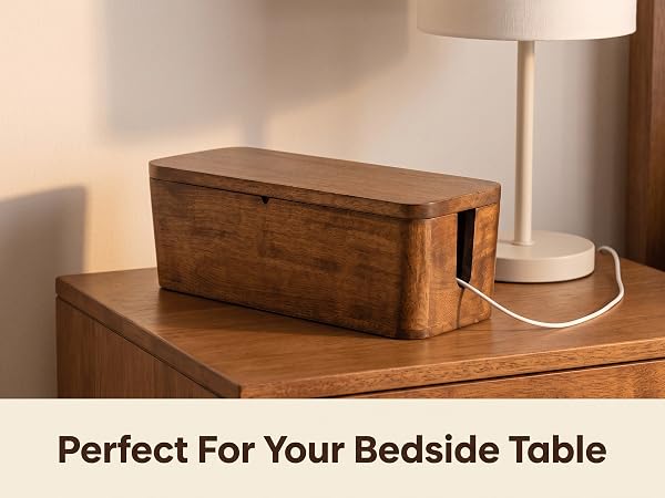 Mango wood cable box by a nightstand holding a phone charger and lamp cord
