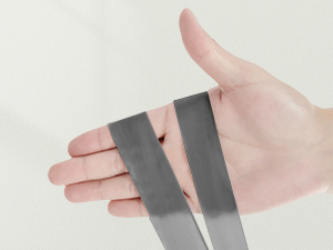 Hand holding two strips of gray, flexible material, demonstrating their bendable nature against a white background.