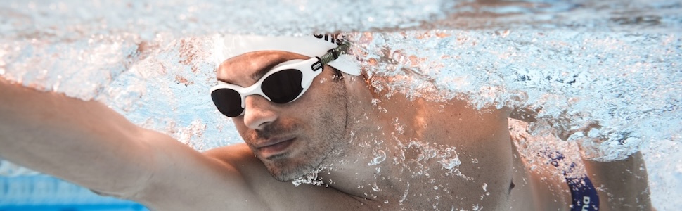 man wearing arena The One Plus swim goggles and arena swim cap in an indoor pool