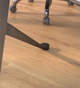 Close-up of office chair casters on a light wooden floor. Three black wheels are visible, with metal stems connecting them to the chair base.