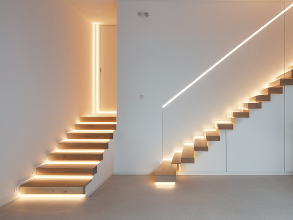 Modern minimalist floating staircase with integrated LED lighting underneath each step, creating dramatic illumination against white walls.