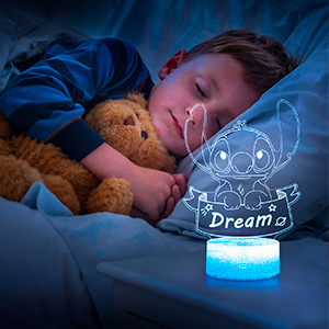 Child sleeping with teddy bear next to a blue glowing night light projecting a cartoon character outline on the ceiling.