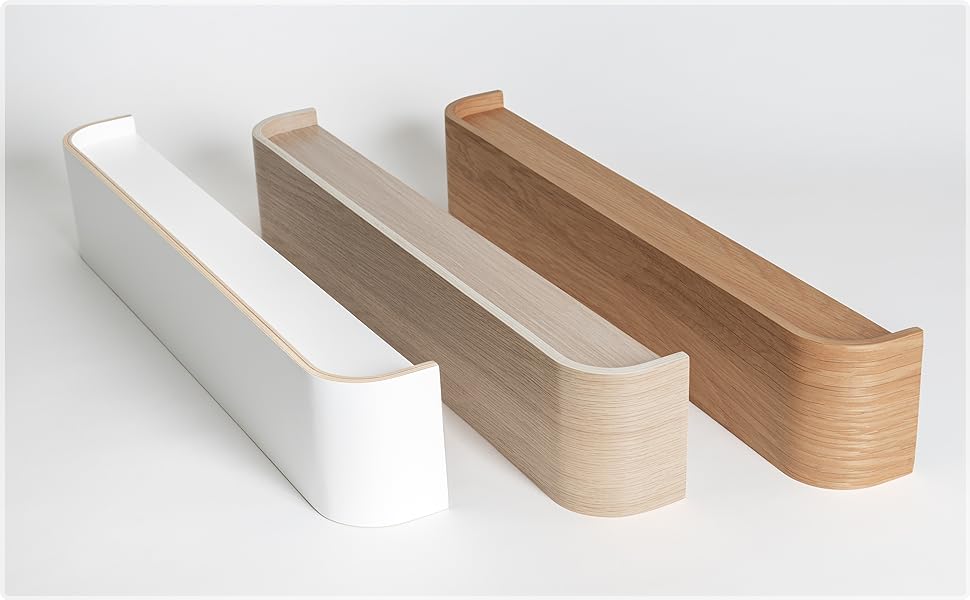 Three minimalist wooden wall shelves in white, light wood, and dark wood finishes. Each shelf has a sleek, L-shaped design with a raised edge.