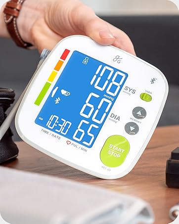Hand holding a Greater Goods Bluetooth Blood Pressure Monitor on a coffee table