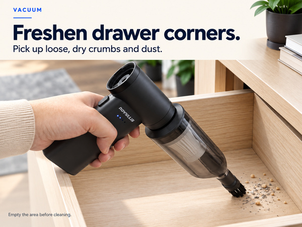 Mini handheld vacuum collecting loose dry crumbs and dust from an empty wooden drawer