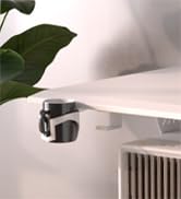 Metal clamp-on cup holder attached to the edge of a light-colored desk or table. Green plant leaf visible in upper left corner.