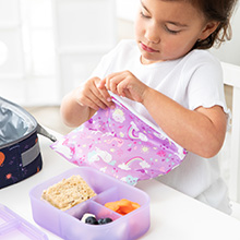 Child sitting at a table with a lunchbox, packed food storage container and zipping a cloth bag