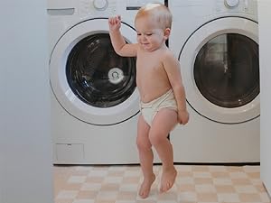 Baby wearing an Inner jumping in front of a washer and dryer