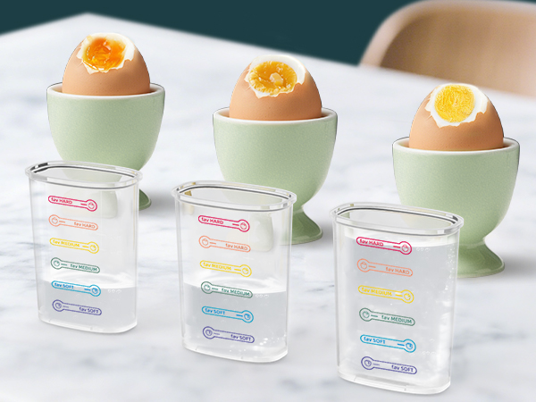 Three pastel green egg cups with soft-boiled eggs, alongside three clear plastic containers with colorful measurement markings for different cooking times.