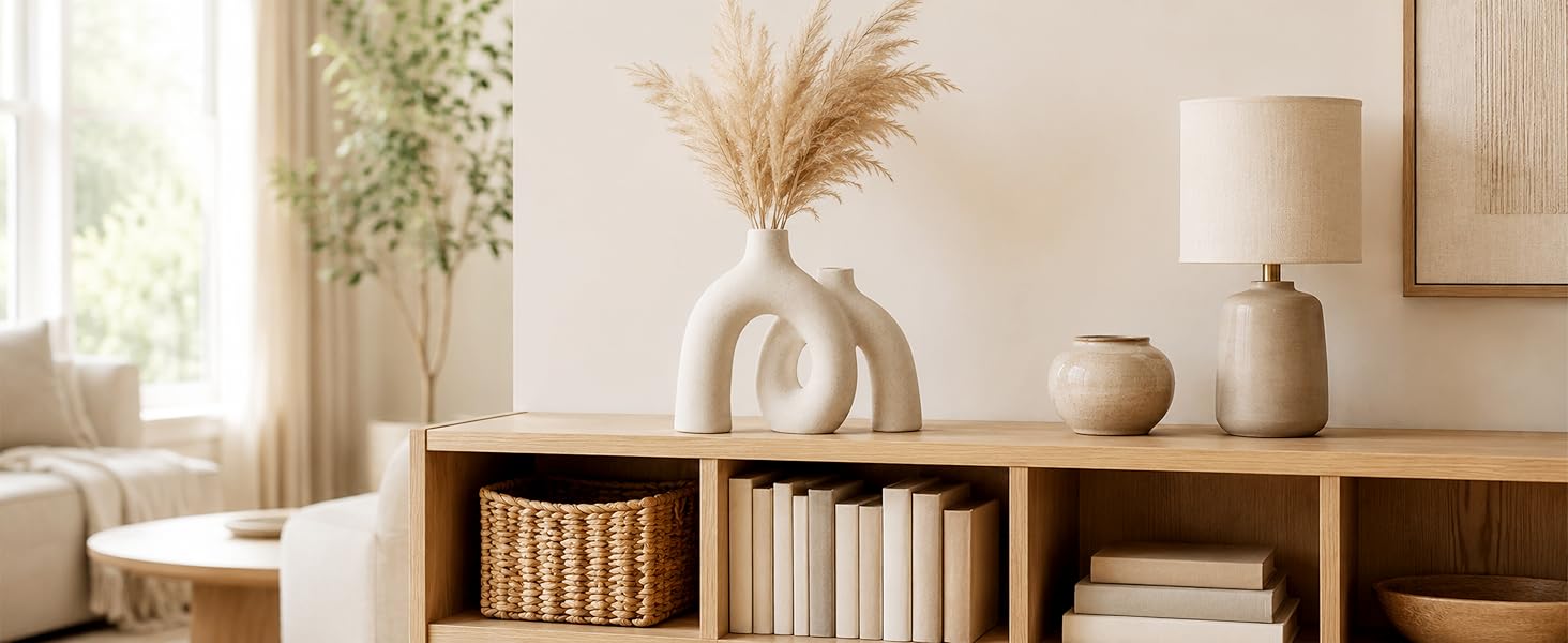 Cream ceramic donut vase with pampas grass displayed on a wooden cabinet in a warm