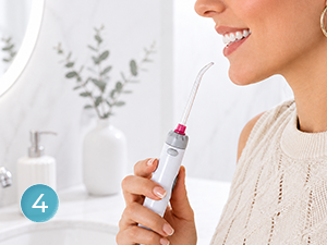 Person in beige sweater holding small spray bottle against neck in bright white interior space with minimalist decor and blue circular marker visible.