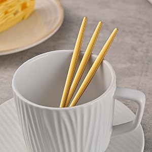 White ribbed ceramic mug shown from different angles with wooden chopsticks or utensils resting on its rim, photographed against a gray surface.