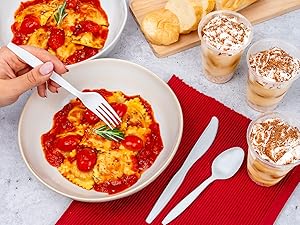 Fork picking up a piece of ravioli. Spoon and knife on side.
