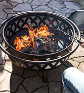 bronze crossweave fire pit with log poker and spark screen on stone patio with roaring fire
