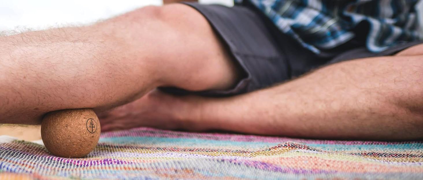 man sitting on mat rolling out calf with rawlogy cork massage ball