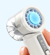 White handheld facial cleansing device with blue circular dial and textured grip held in person's hand against light blue background. Compact electrical skin care tool.
