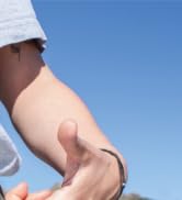 Person's arm wearing a smartwatch or fitness tracker against clear blue sky background, demonstrating wearable device on wrist.