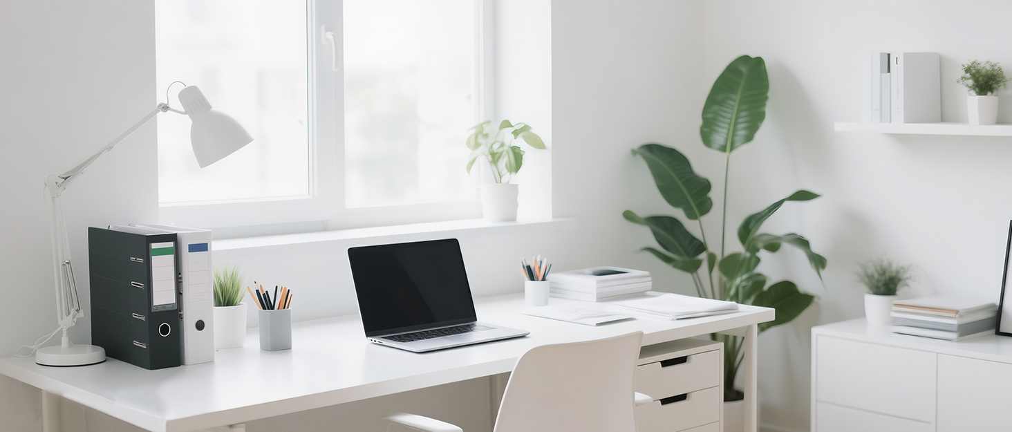 Minimalist home office setup with white desk, laptop, desk lamp, file organizer, and potted plants. Bright room with large window and white walls.