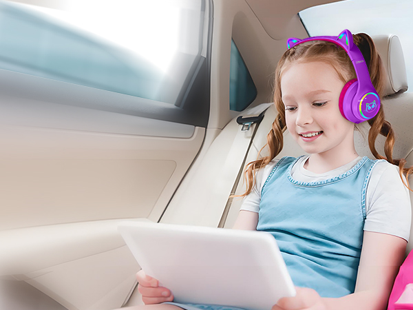 Purple over-ear headphones worn by a child in a car seat. The child is looking at a white tablet device held in their hands.