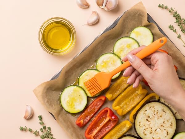 Orange silicone oil brush coating vegetables with olive oil before roasting on peach background