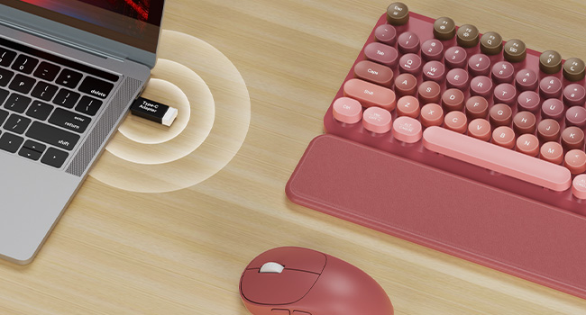 USB receiver plugged in laptop connects pink wireless keyboard mouse combo with wrist rest on desk