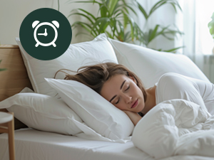 A person sleeping peacefully in a white bed with fluffy pillows and comforter. A clock icon is visible in the top left corner.