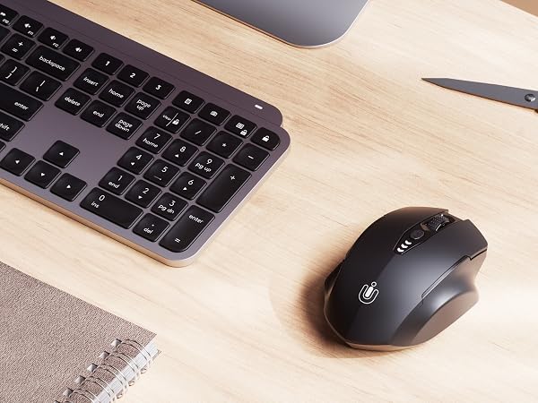 Desktop workspace with wireless keyboard, mouse, and calculator on light wooden surface.