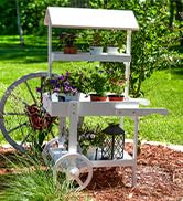 White flower cart in lush backyard filled with flowers and small plants and garden decor in summer