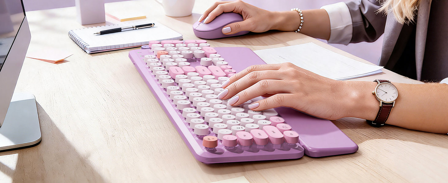 Typing on a lavender purple retro wireless keyboard with matching mouse on a bright office desk.