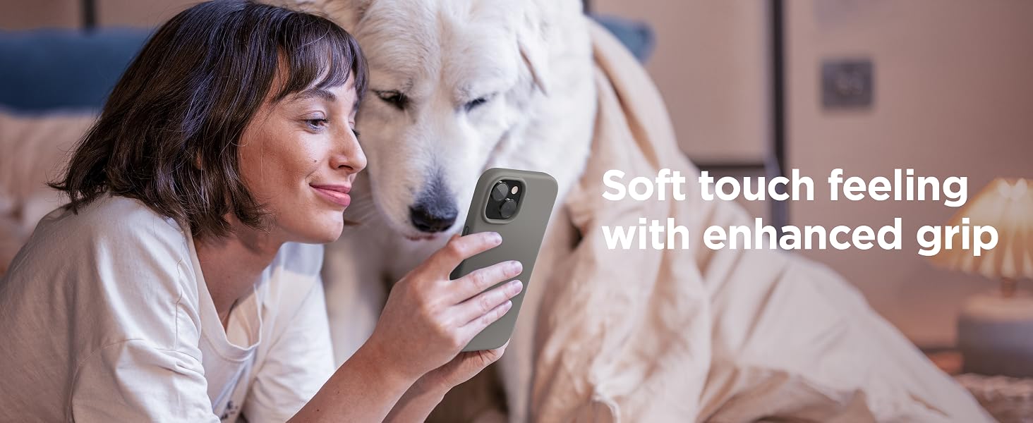 Woman holding gray smartphone with enhanced grip feature, emphasizing soft touch feeling. White dog visible next to her.