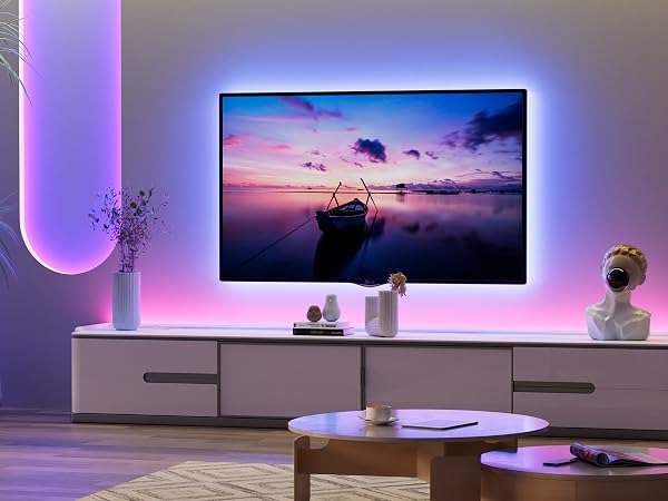 Large flat-screen TV with ambient backlighting displaying sunset scene. TV mounted above white cabinet in modern living room with purple-tinted lighting and decorative items.