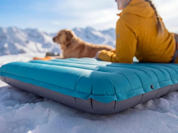 Side view of thick Airlive2000 pad on snow as users lounge with dog.
