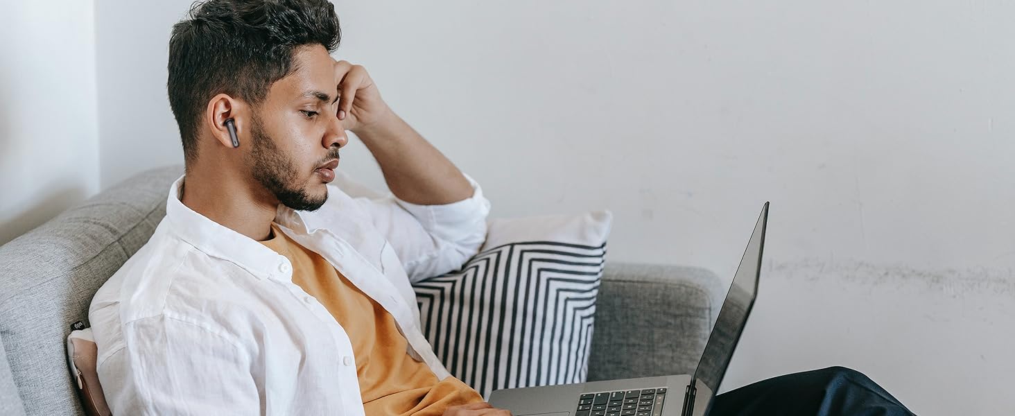 man sitting on a couch with his head in his hand and looking at a laptop