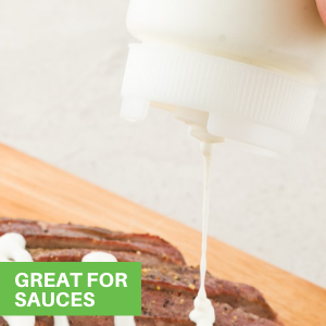 A person using a clear squeeze bottle with white lid to dispense sauce onto food.