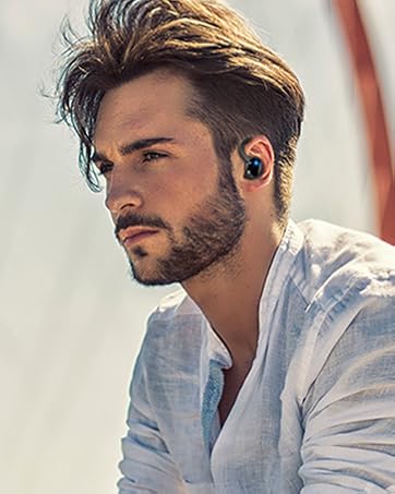 Wireless earbud in ear of person with styled hair and beard, wearing light-colored shirt. Close-up view emphasizes the earbud's compact design.