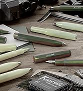 Collection of mint green and sage colored fountain pens and writing instruments scattered on wooden surface. Text visible includes 'Kaweco' on a dark card.