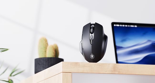 Desktop setup with a wireless computer mouse and laptop screen visible, alongside decorative plants on a white surface.