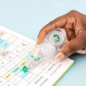 Hand holding a correction tape applicator to edit a calendar.
