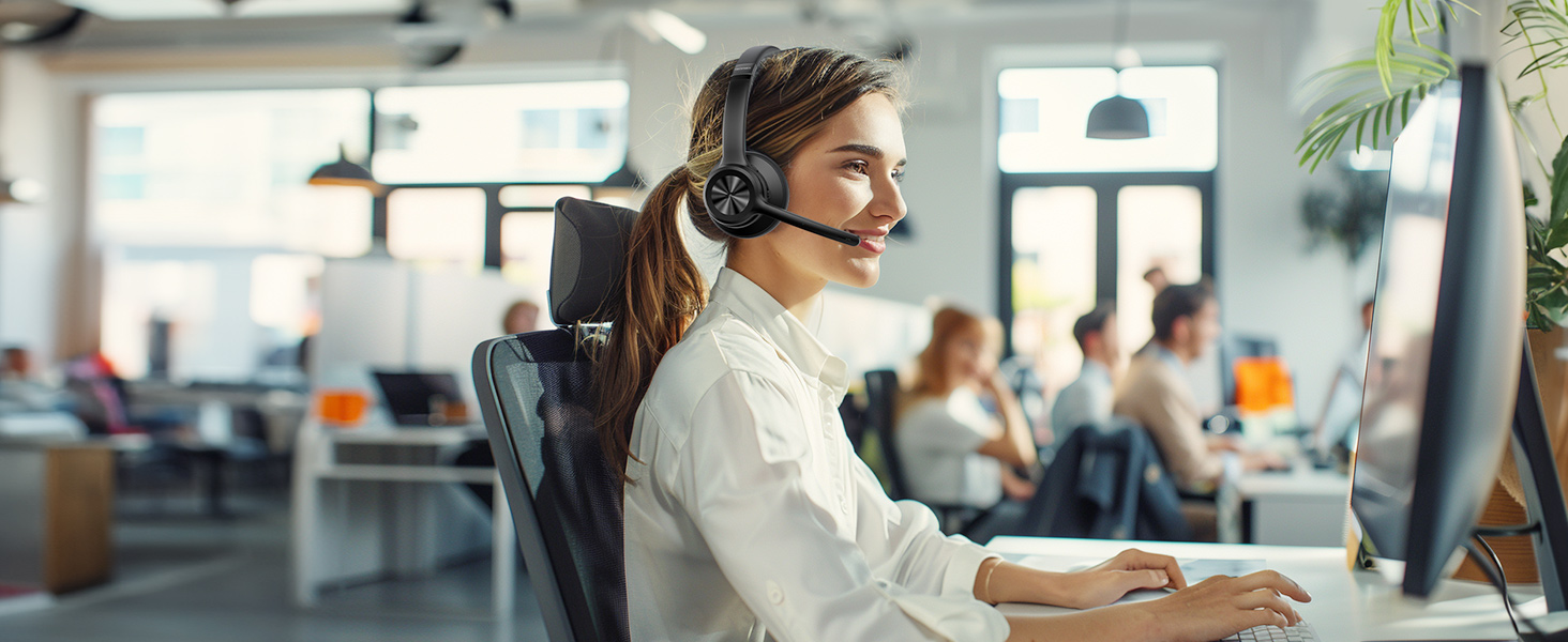 Customer service representative at computer workstation wearing wireless headset in open office environment.