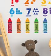 Educational number line display showing colorful crayon-shaped markers numbered 1 through 8, with stuffed animal toy visible at bottom.