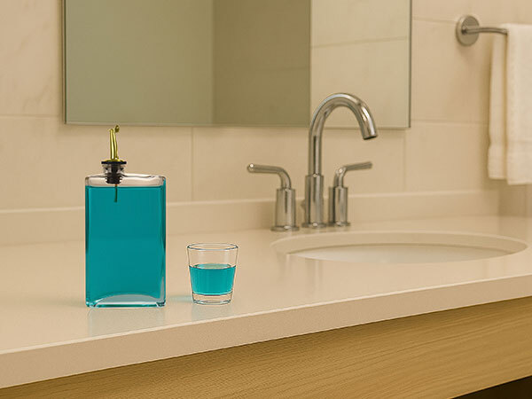Glass dispenser filled with blue mouthwash next to a small glass on bathroom counter